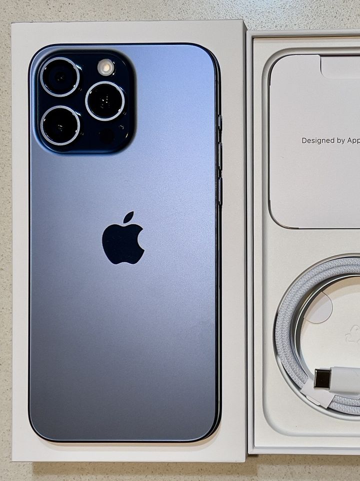 iPhone 15 Pro Max w kolorze tytanu błękitnego obok otwartego pudełka z kablem USB-C